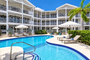 Ein Hotel mit Poolbereich, mehreren Balkonen und Außenbestuhlung mit Sonnenschirmen.
