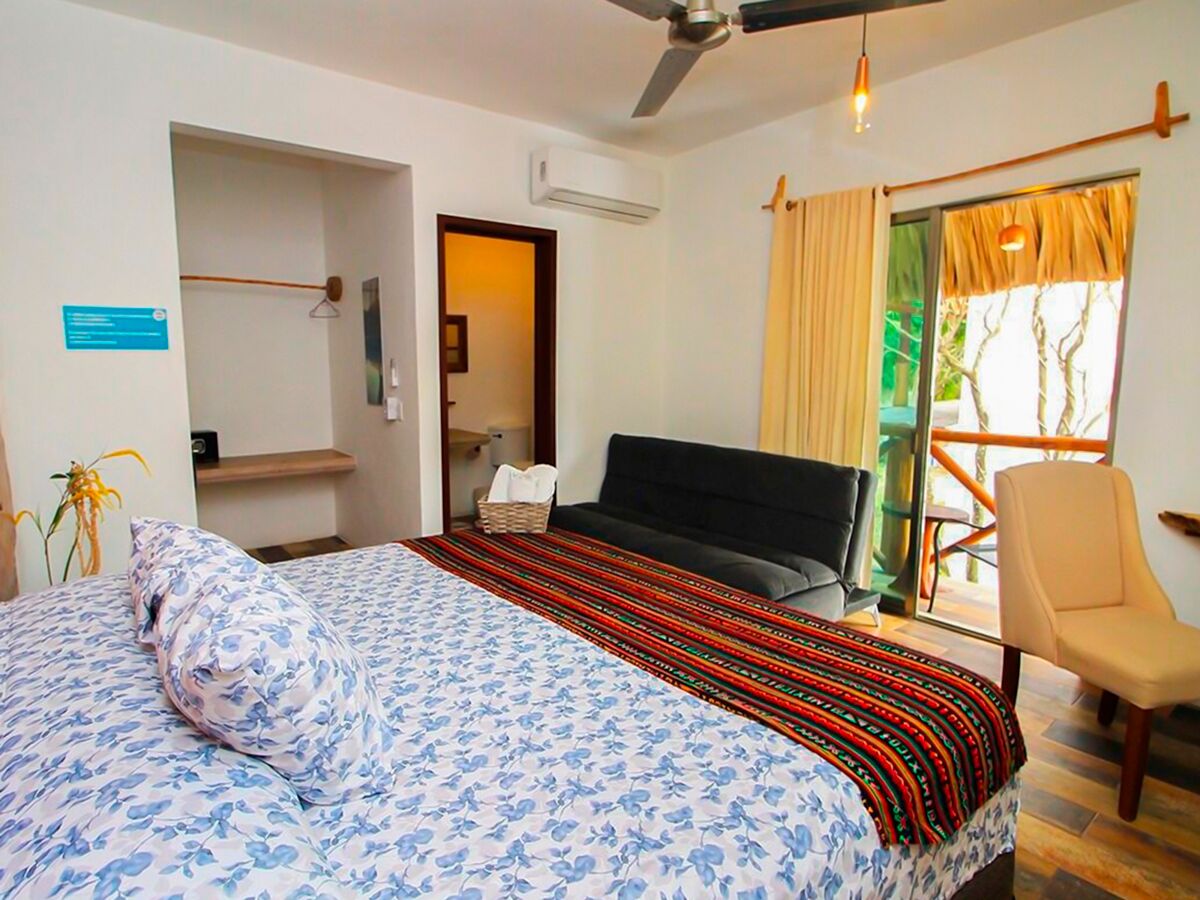 A hotel room with a bed, a chair, a desk, and a window with curtains.