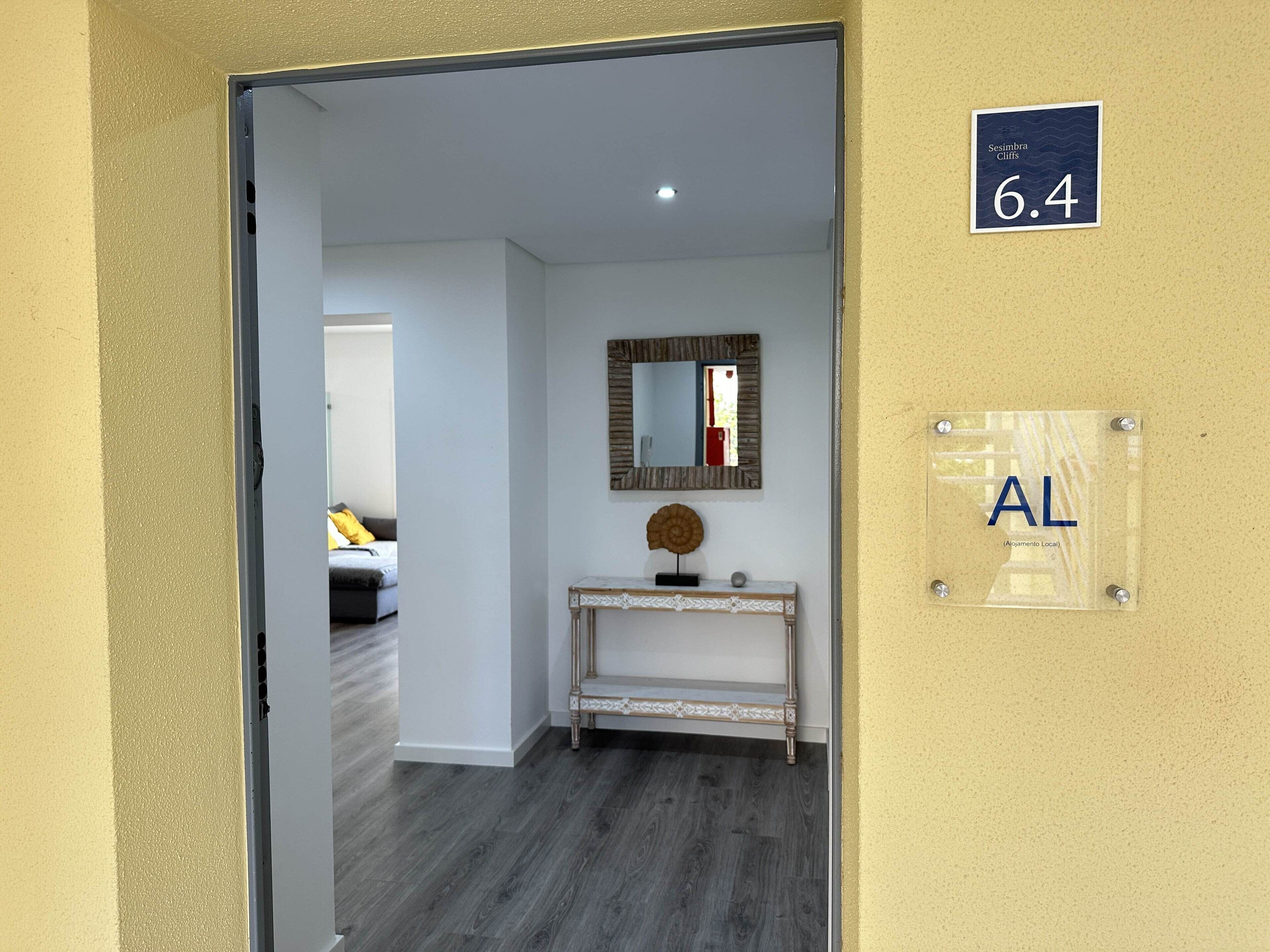 Een hotelkamer met een houten vloer, een witte console tafel met een spiegel erboven en een bordje met het kamer nummer 6.4.