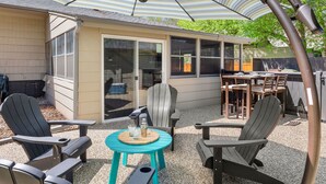 An outdoor patio with Adirondack chairs, a round table, and a striped umbrella. - Historic Mountain Ave Bungalow – Walk Everywhere! (Fort Collins)