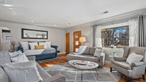 A modern living room with a blue sofa, grey armchairs, and a white coffee table. - Historic Mountain Ave Bungalow – Walk Everywhere! (Fort Collins)