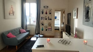 Een moderne woonkamer met een grijze bank, een witte salontafel en een keuken met een wit aanrecht.