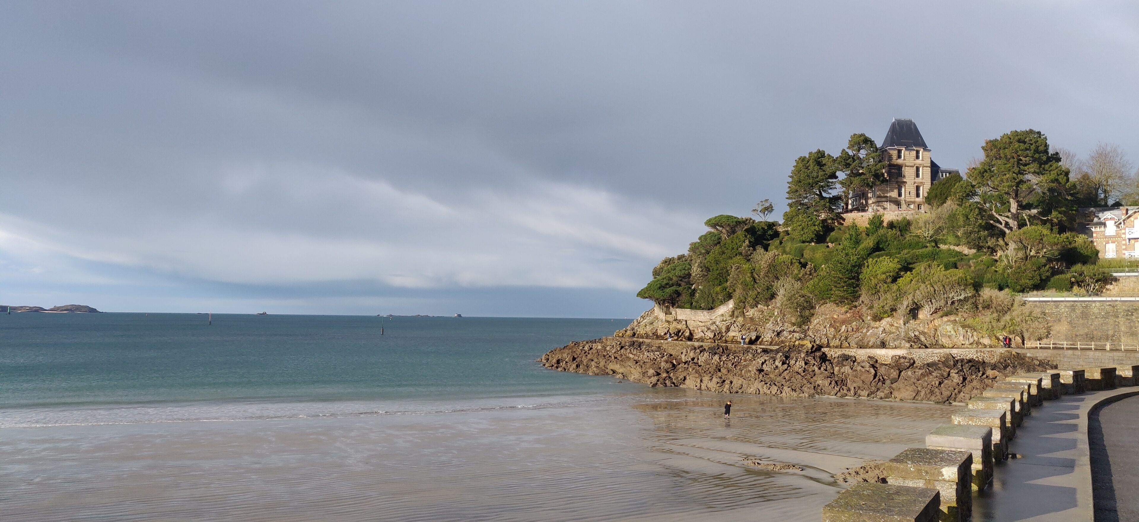 Une vue côtière avec un bâtiment historique perché sur une falaise, un rivage rocheux et une mer calme.
