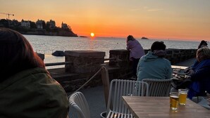 Zonsondergang vanaf een terras met stenen hekwerk, een tafel met stoelen en enkele zittende personen.