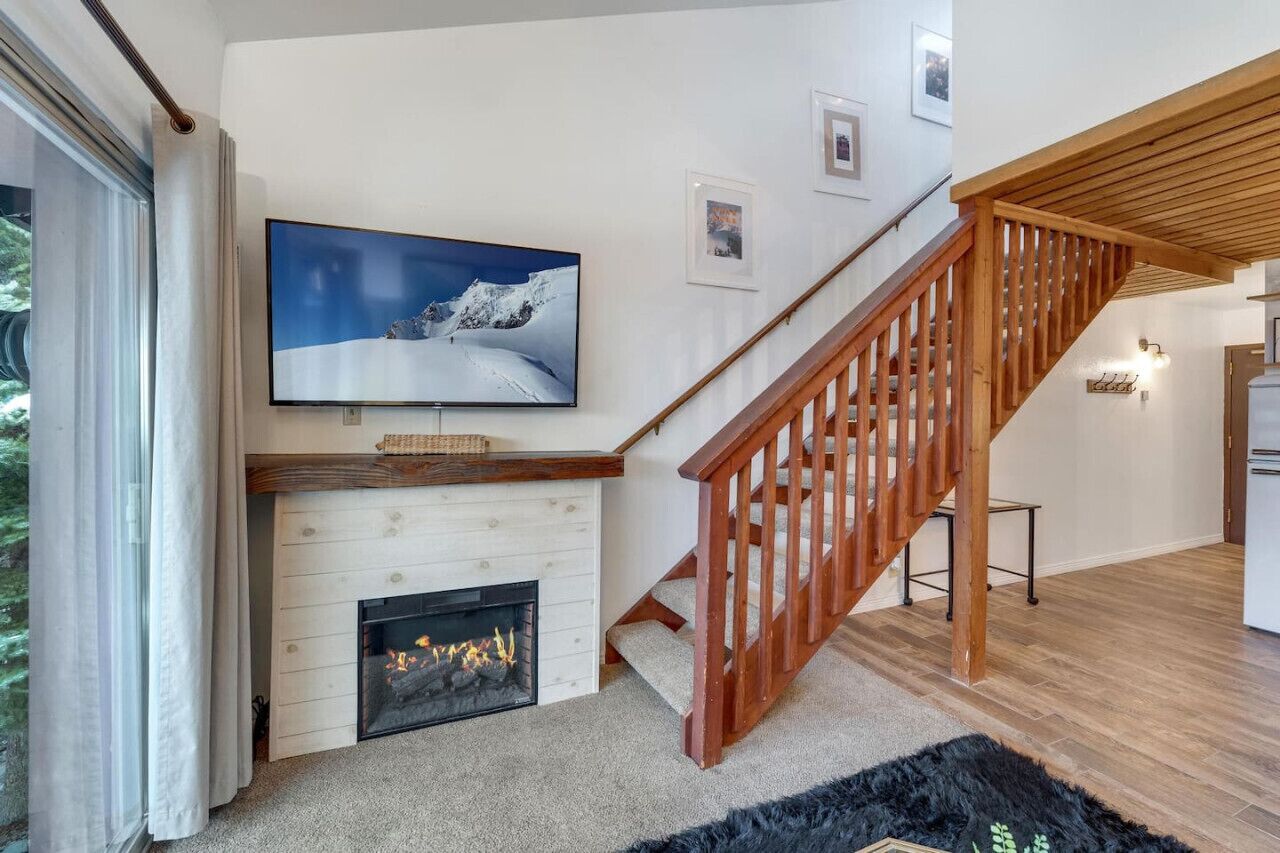 Un salon moderne avec une cheminée, un escalier en bois et un grand téléviseur à écran plat fixé au mur.