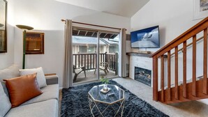 Een woonkamer met een bank, een glazen salontafel, een open haard, een televisie en een balkon met uitzicht.