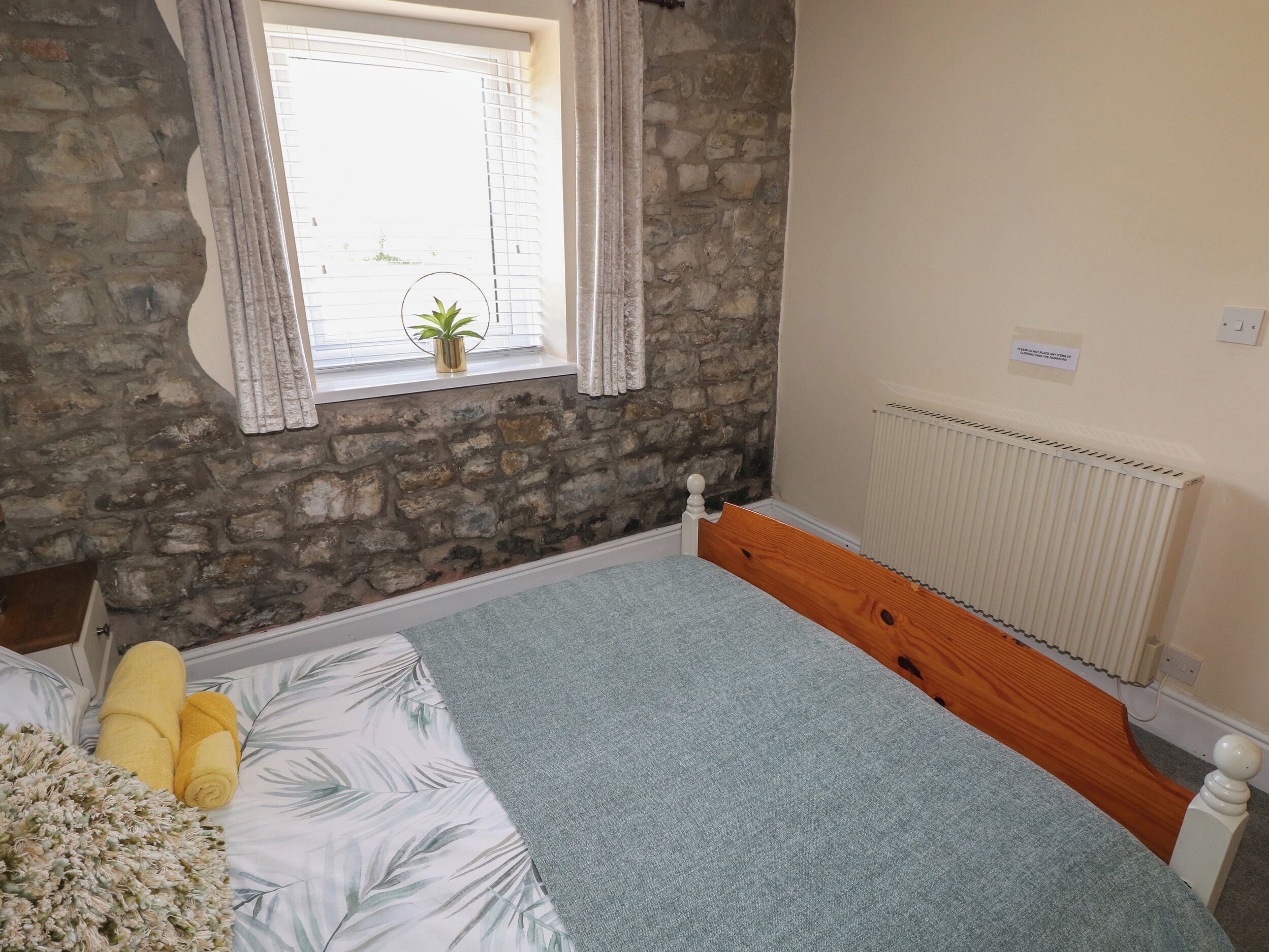 Ein Schlafzimmer mit Steinsturz, einem Fenster mit Vorhängen, einem Heizkörper und einem Bett mit grauer Decke und Kissen.