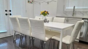 A modern kitchen with white cabinetry, a stainless steel sink, and a dining area with white chairs and a table.