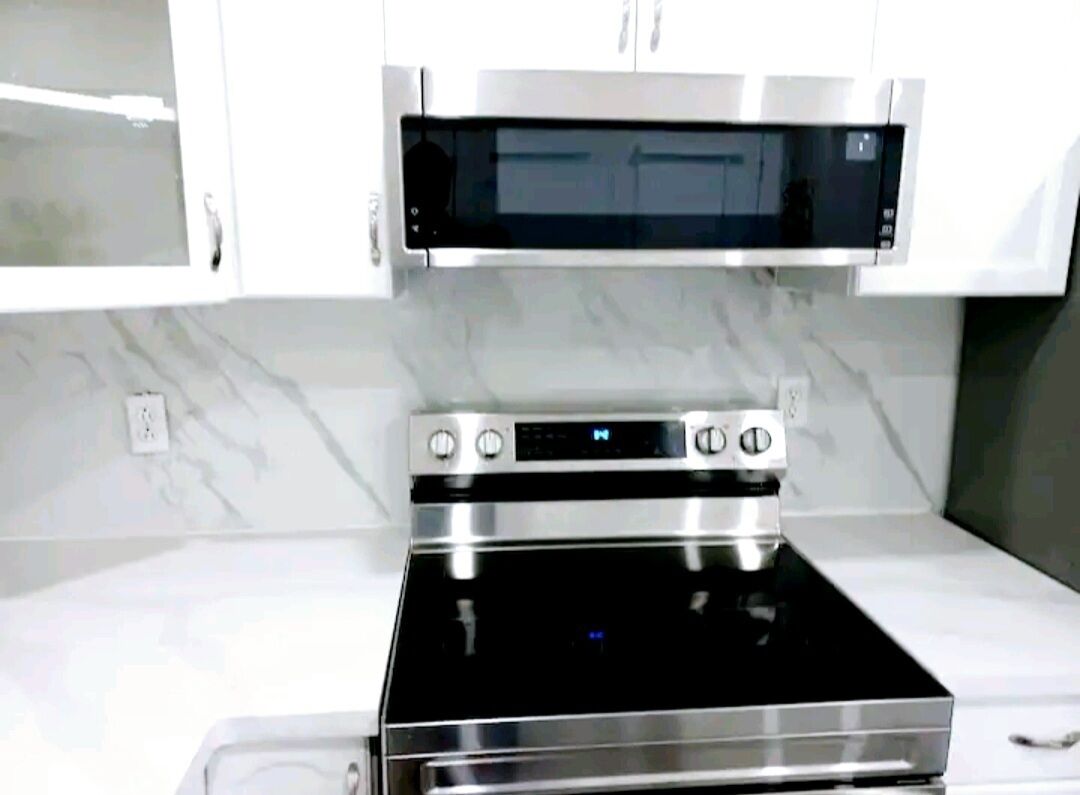 A kitchen with a built-in oven and microwave, white cabinets, and a marble backsplash.