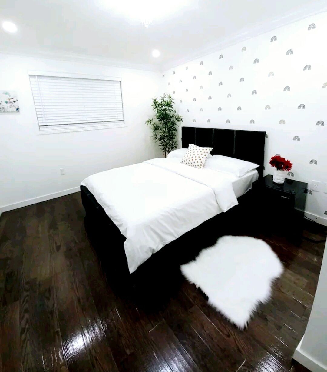 Ein Schlafzimmer mit einem Bett, einem Nachttisch, einer Pflanze und einem weißen, flauschigen Teppich.