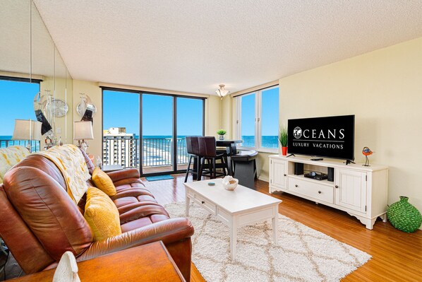 A spacious living room with a leather sofa, a white coffee table, and a television on a white cabinet. - Oceanfront Penthouse-Heated Pool-Oceans 3 #2206 (Daytona Beach Shores)