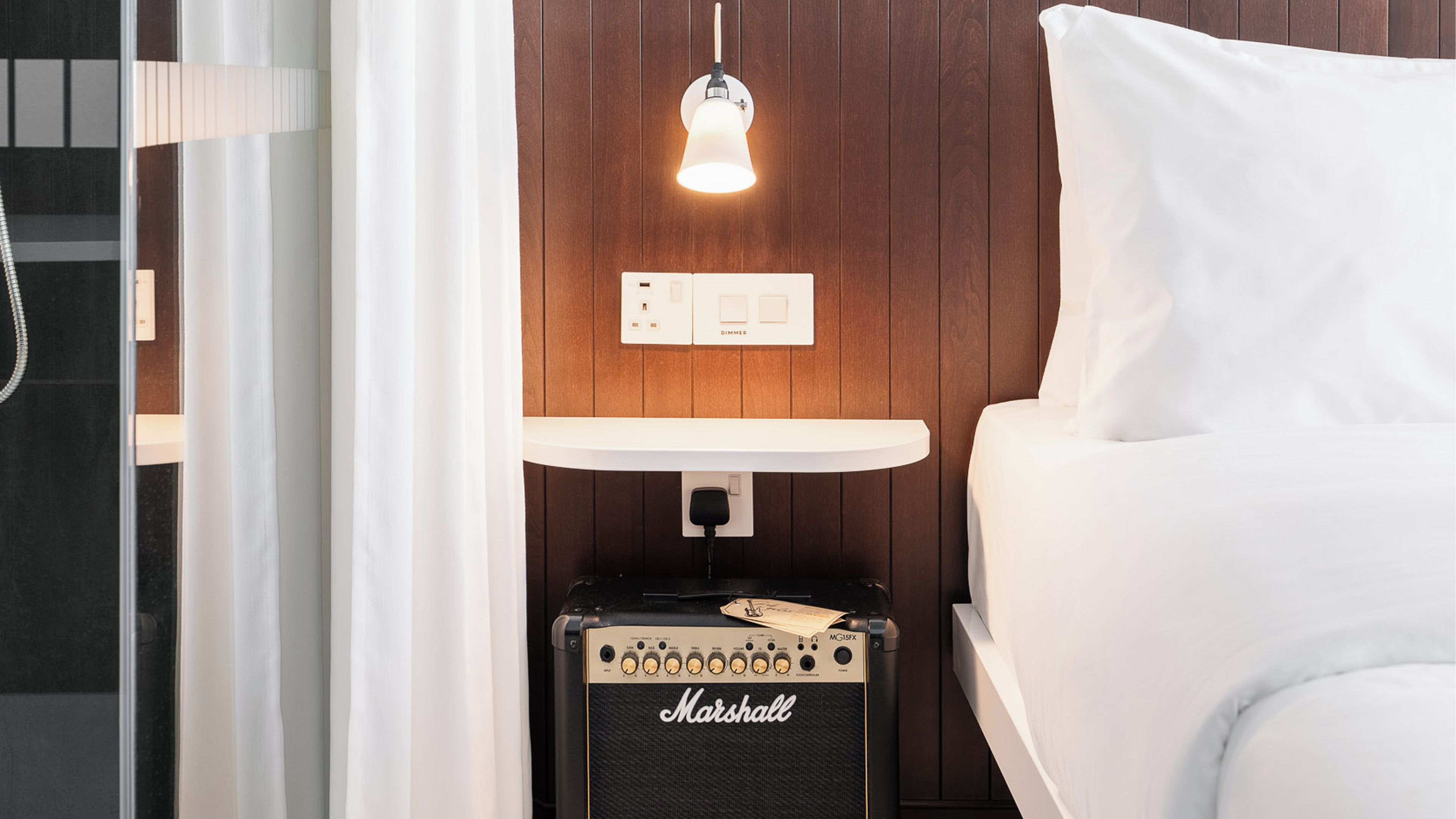Hotellihuone, jossa on sänky, yöpöytä, jossa on Marshall-vahvistin, himmennin ja riippuvalaisin.
