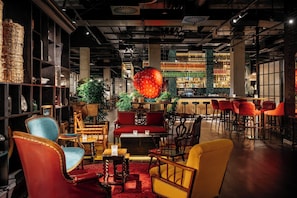 A bar area with a large red fruit centerpiece, wooden furniture, and a variety of bottles on shelves.