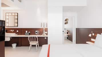 A hotel room with a bed, a desk with a chair, a vanity with a mirror, and a television.