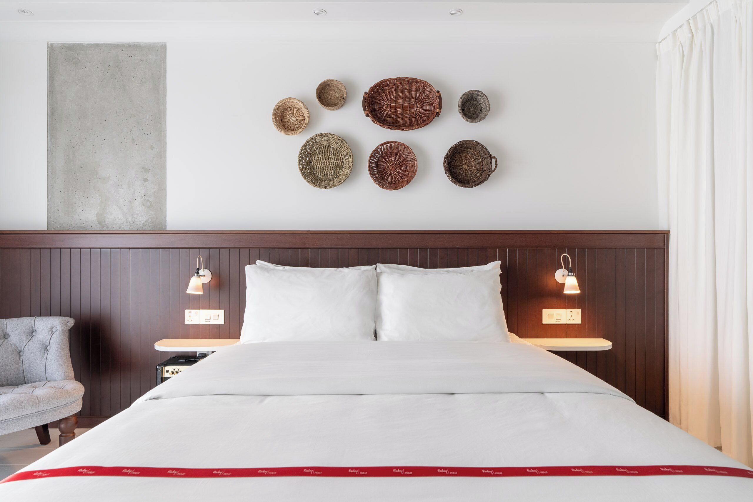 Habitación de hotel con una cama grande, dos mesitas de noche, una silla y cestas decorativas fijadas a la pared.