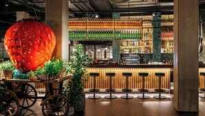 A bar area with a large red spherical decoration, wooden stools, and a variety of bottles on shelves.