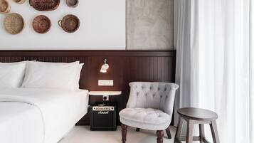 A neatly arranged bedroom with a bed, a chair, a stool, a nightstand with a lamp, and a wall-mounted basket collection.