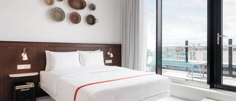 Une chambre d’hôtel moderne dotée d’un grand lit, offrant une vue sur la ville et comprenant un balcon avec des meubles d’extérieur.