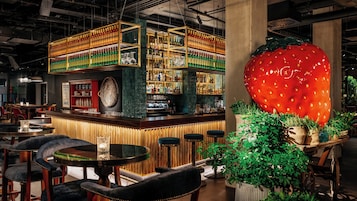 Zona de bar con estantes llenos de botellas, una gran decoración de fresa y asientos.