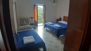 Ein Hotelzimmer mit zwei Betten, einem Heizkörper, einem Sessel und Blick auf Grün durch das Fenster.