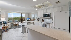 A modern kitchen with white cabinetry, a large island, and a dining area with a view.