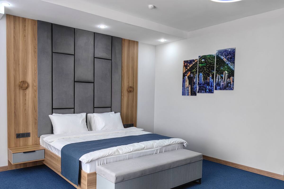 Un dormitorio moderno con una cama, un banco y un cuadro con vista a la ciudad.