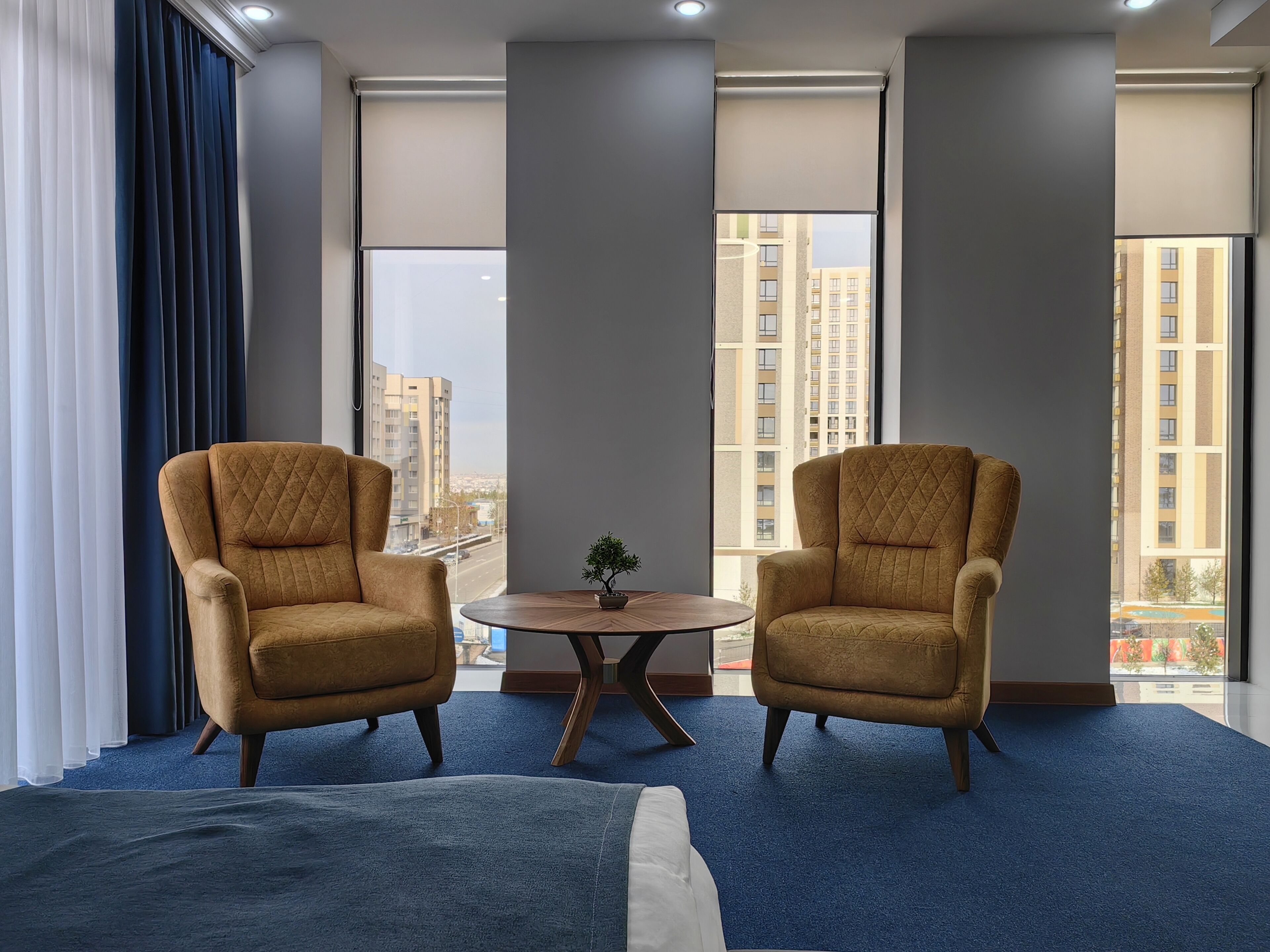 A hotel room with two armchairs, a small round table with a plant, and a bed.
