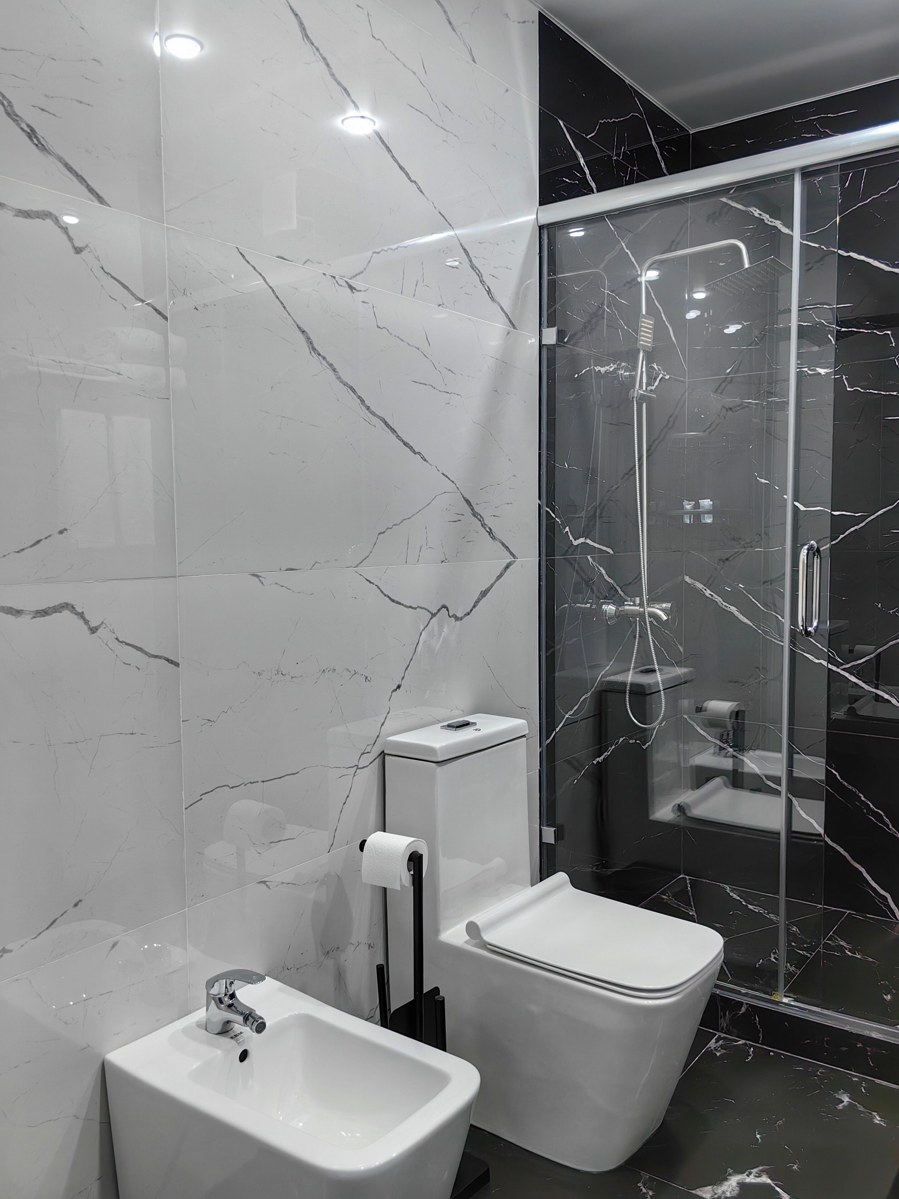 Een moderne badkamer met een marmeren spatwand, een glazen douchecabine en een witte wastafel.