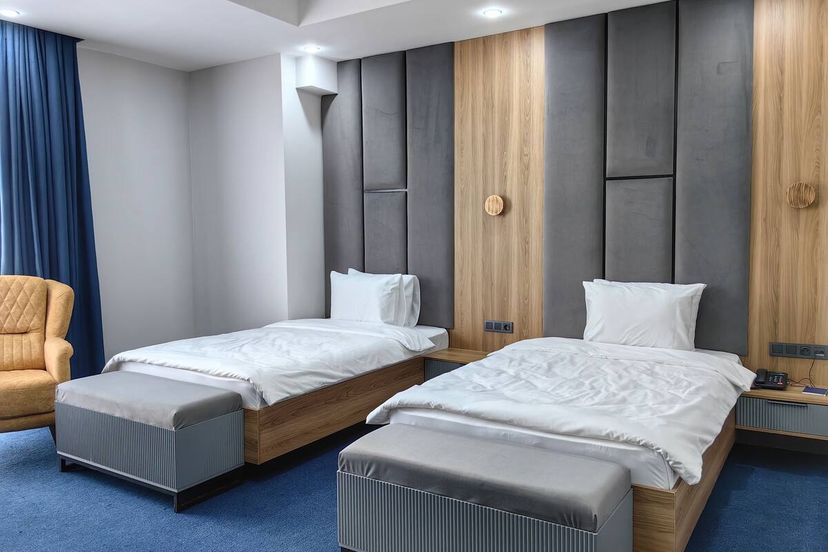 Habitación de hotel moderna con dos camas individuales, una pared de acento de madera, alfombra azul y una mesita de noche con un teléfono.