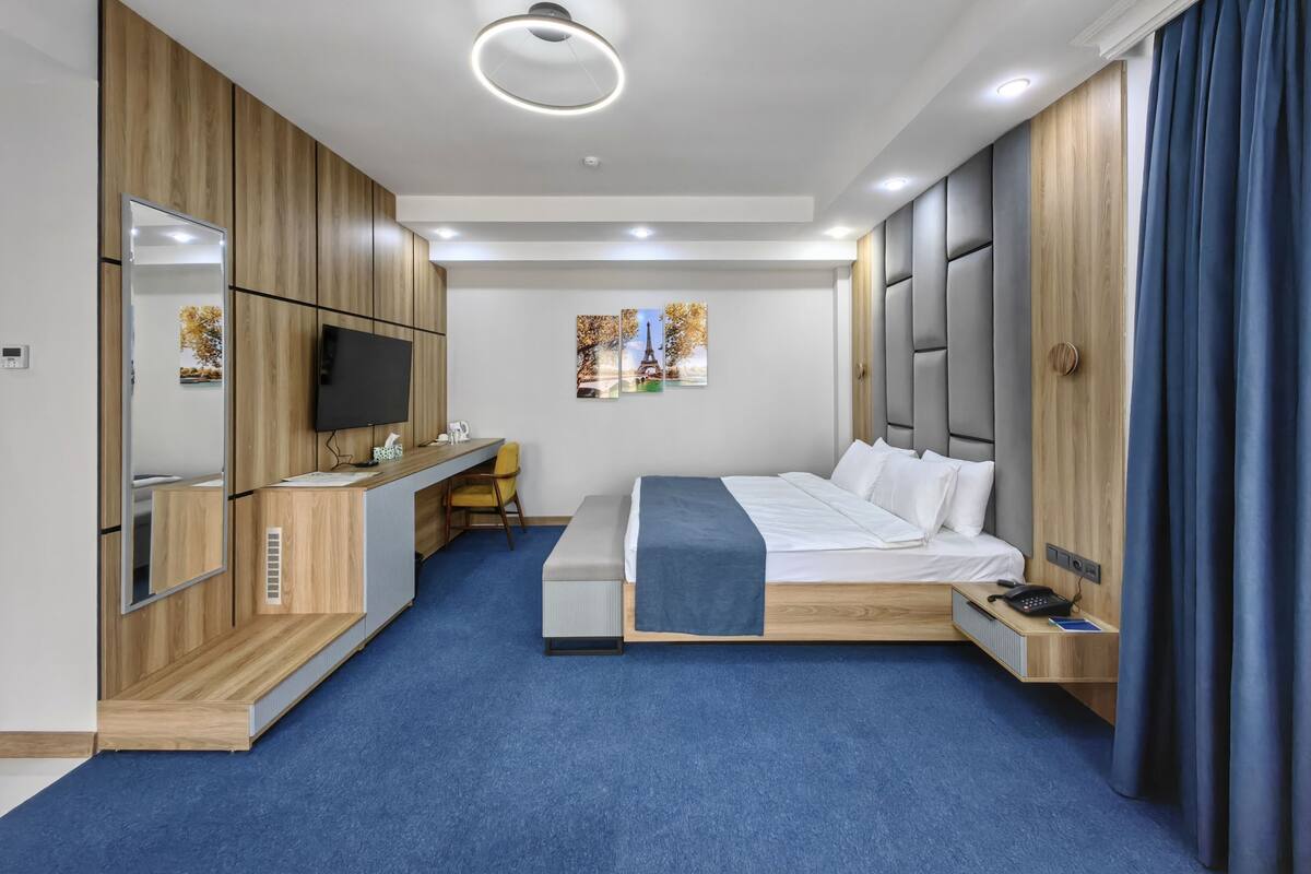 Una habitación de hotel moderna con una cama, un escritorio, un televisor y un espejo grande.