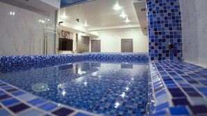 A modern indoor swimming pool with blue mosaic tiles, a glass wall, and a ceiling with recessed lighting. - Shymkent Park Hotel (Shymkent)