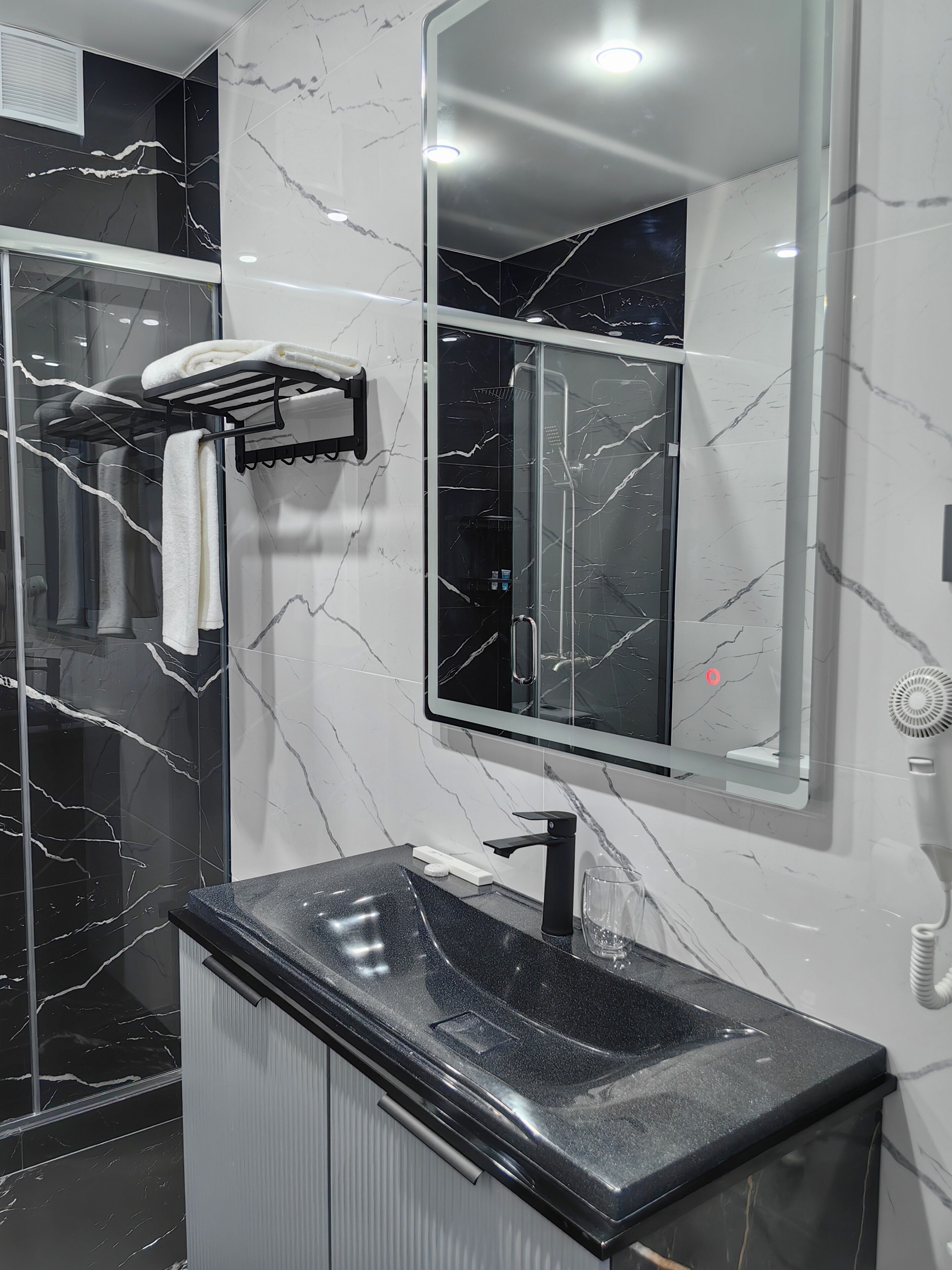 Un baño moderno con tocador de mármol negro, cabina de ducha de vidrio y un espejo grande.