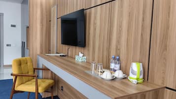 Un mostrador de recepción con un televisor de pantalla plana, una silla amarilla, una caja de pañuelos, botellas de agua y un botiquín de primeros auxilios.