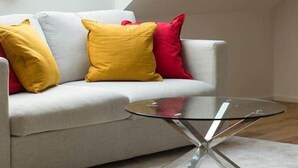 A modern loft bedroom with a sloped ceiling, a grey sofa with yellow and red cushions, and a glass coffee table. - Modernes Apartment im Zentrum der Stadt (Graz)