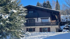 Eine zweistöckige Lodge mit Balkon, umgeben von schneebedeckten Bäumen.