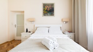 Una habitación de hotel con una cama bien hecha, un cuadro en la pared y una mesita de noche con una lámpara y una botella.