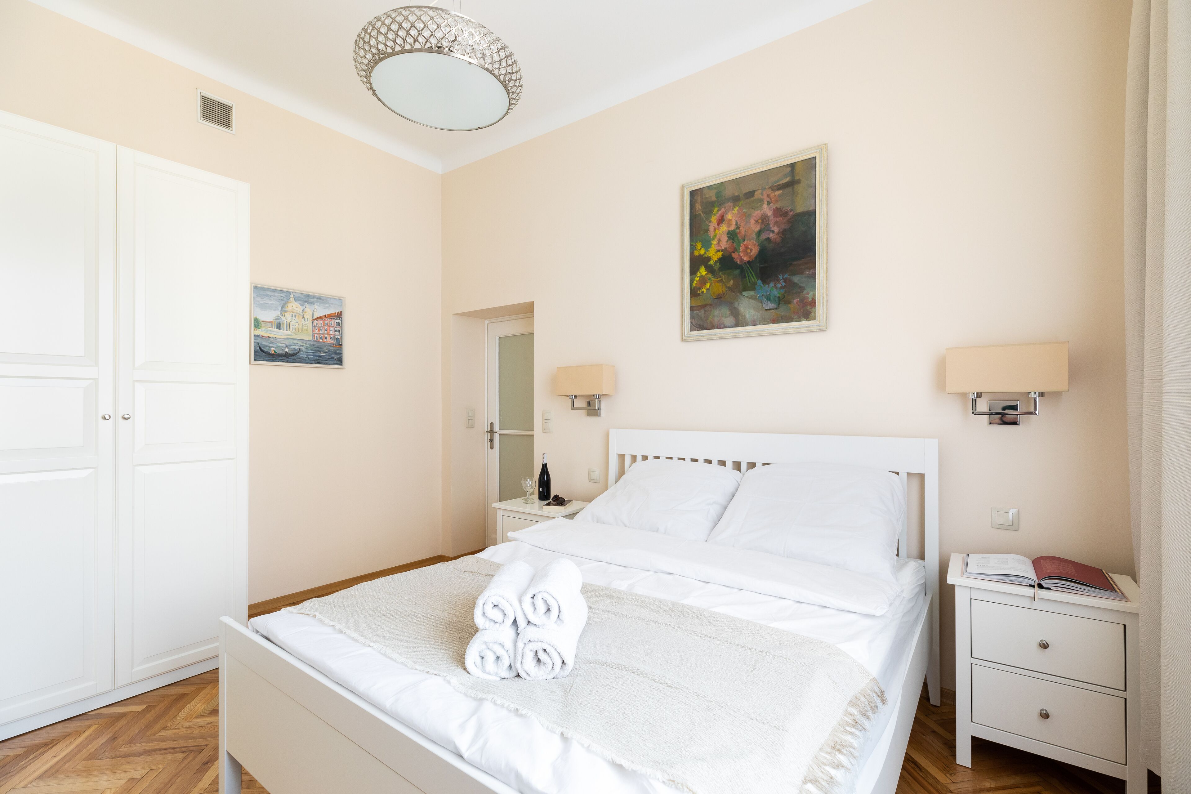 Un dormitorio ordenado con cama, mesitas de noche, un armario y un cuadro en la pared.