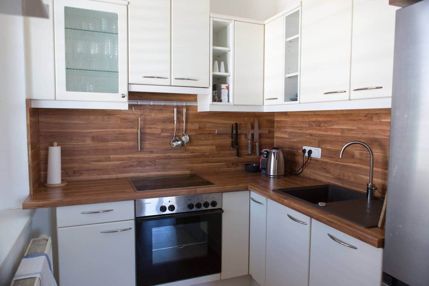 A compact kitchen with white cabinets, a stainless steel oven, a sink, and wooden countertops.