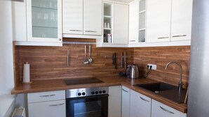 Een kleine keuken met witte kastjes, een roestvrijstalen oven, een spoelbak en houten aanrechtbladen.
