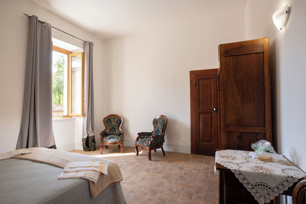 A bedroom with a bed, two chairs, a wooden door, and a table with a tablecloth.