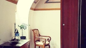 A room with a wooden chair, a small table with a lamp and a plant, and a door. - Locanda di Posta (L'Aquila)