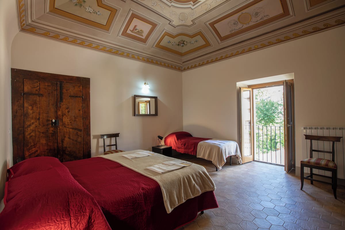 A room with two beds, a wooden wardrobe, a small table, and a bench.