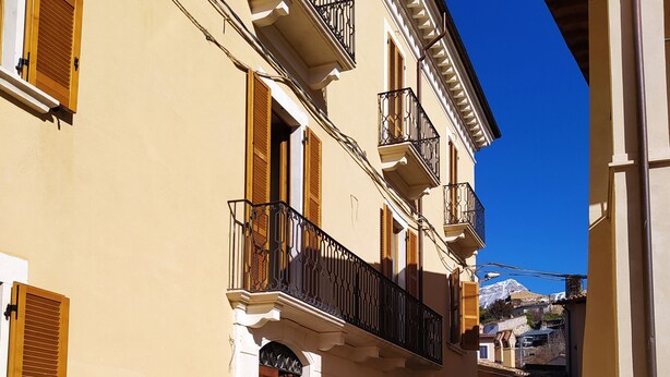 A narrow cobblestone street flanked by buildings with balconies and wooden shutters. - Locanda di Posta (L'Aquila)