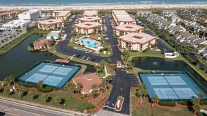 Un complejo turístico con múltiples canchas de tenis, piscina y vistas a la playa.