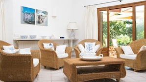 Una habitación con muebles de mimbre, una mesa de centro y vistas a través de un ventanal.