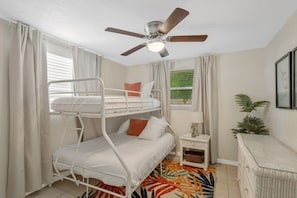 A bunk bed room with a ceiling fan, a small table with a lamp, and a wicker chair.