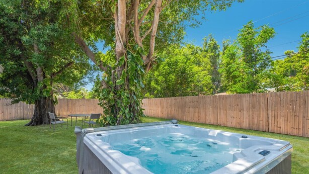 A hot tub in a backyard with a wooden fence, a tree, and a lawn.
