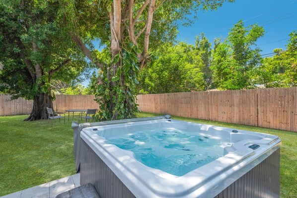 Un bain à remous dans un jardin, avec une clôture en bois, un arbre et une pelouse.
