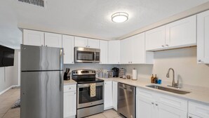 A modern kitchen with stainless steel appliances, white cabinets, and a tiled floor.