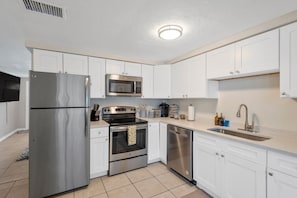 A modern kitchen with stainless steel appliances, white cabinets, and a tiled floor.